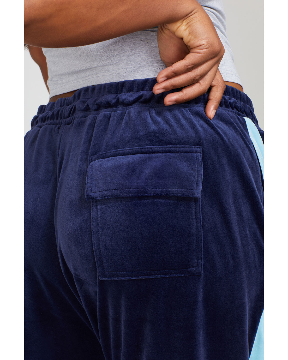 Detail shot of back pocket shows plus sized model wearing navy blue velour sweatpant with color blocked light blue stripe down both sides. 