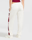 Back view image of standard sized model shown wearing off white velour sweatpant with color blocked burgundy stripe down both sides. Sweatpant features oversized flap pocket on rear right side. Model has her left hand in her pocket.