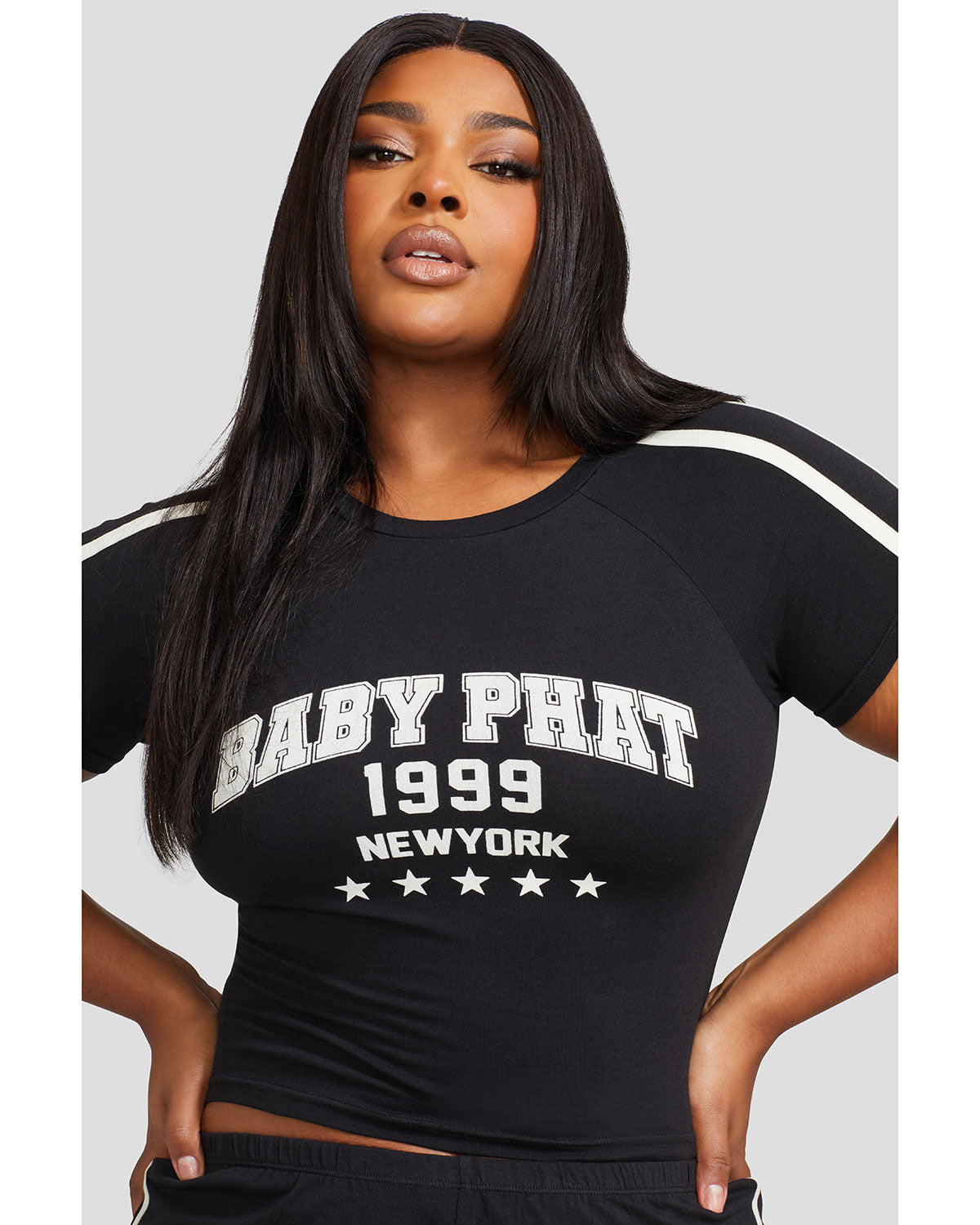 Plus sized model shown wearing black baby tee shirt with Baby Phat logo, New York, 1999, and stars on the center front. Shirt features off white stripes on the shoulder.