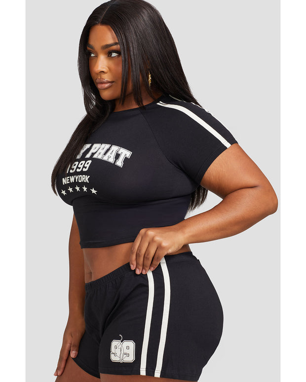 Plus sized model shown wearing black baby tee shirt with Baby Phat logo, New York, 1999, and stars on the center front. Shirt features off white stripes on the shoulder. Model is also wearing matching micro shorts with side stripes and a 99 cat logo.