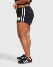 Side view image of plus sized model’s legs shown wearing black micro short with 2 contrasting off white stripes down both sides. Short features off white Baby Phat cat 99 heritage logo on wearer's left thigh. 
