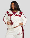 Plus sized model shown wearing off white velour zip up hoodie with color blocked burgundy panel down both sleeves. Zippered sweatshirt features burgundy Baby Phat script logo across upper chest and oversized solid cat logo on wearer's right front. Model is also wearing matching off white sweatpant with burgundy color blocking. 