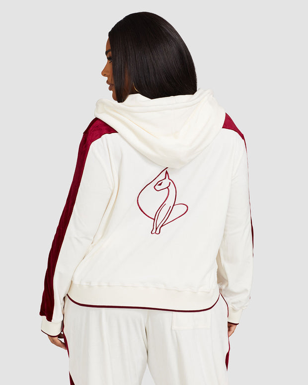 Back view image of plus sized model wearing off white velour zip up hoodie with color blocked burgundy panel down both sleeves. Zippered sweatshirt features matching off white ribbing at the wrists and hem with burgundy tipping. Model is also wearing matching off white sweatpant with burgundy color blocking. 