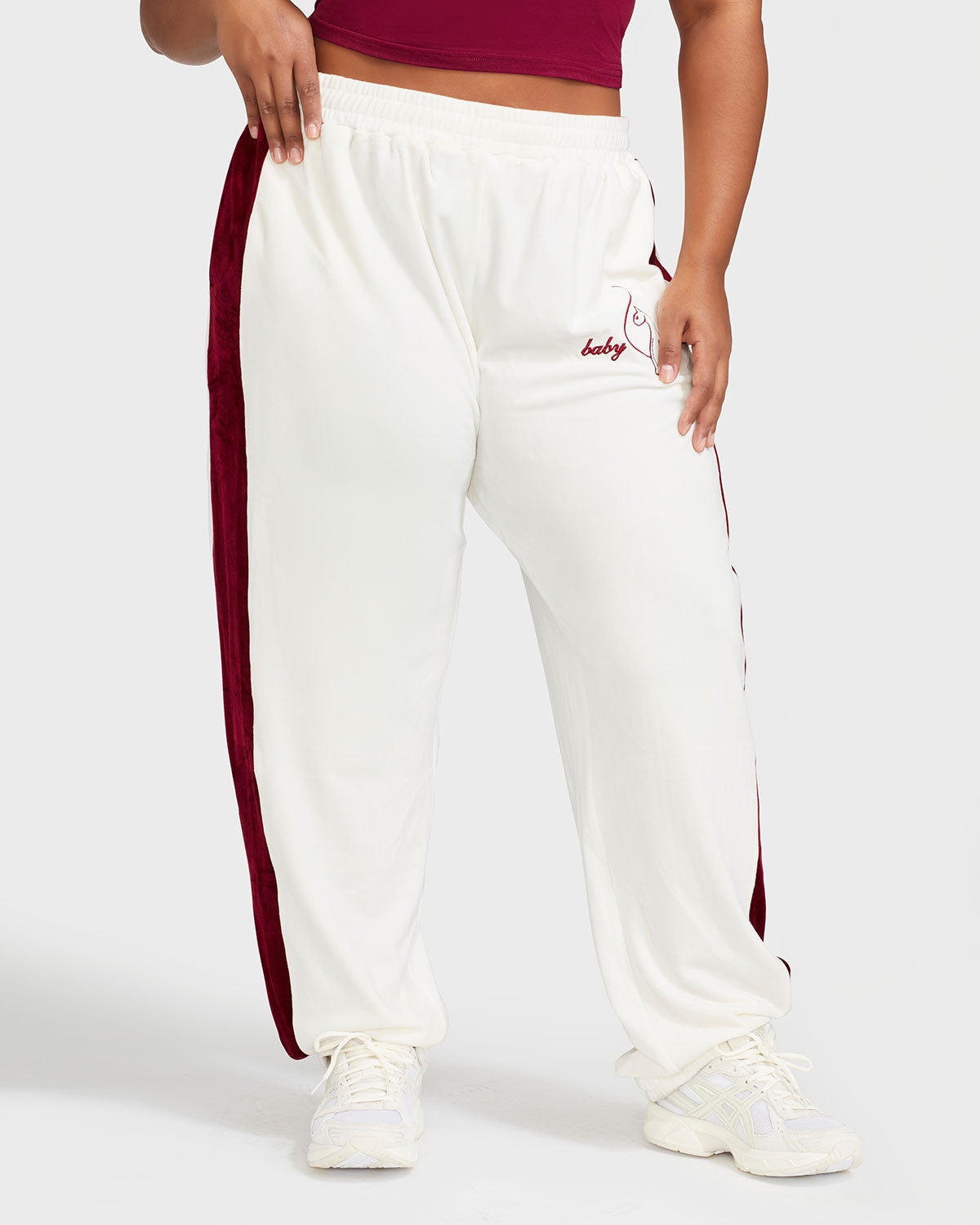 Plus sized model shown wearing off white velour sweatpant with color blocked burgundy stripe down both sides. Sweatpant features embroidered Baby Phat script and cat logo on wearer's upper left thigh. 