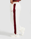 Side view image of plus sized model wearing off white velour sweatpant with color blocked burgundy stripe down both sides. Sweatpant features embroidered Baby Phat script and cat logo on wearer's upper left thigh. 