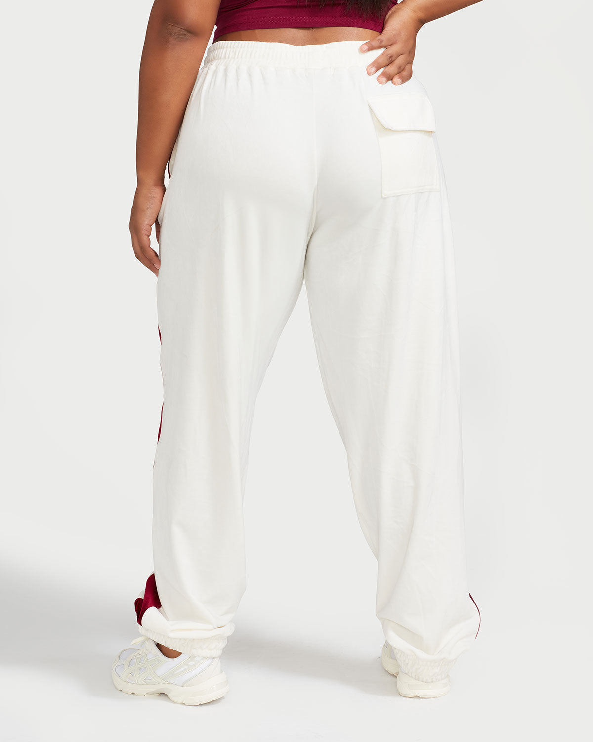 Back view image of plus sized model wearing off white velour sweatpant with color blocked burgundy stripe down both sides. Sweatpant features oversized single pocket on rear right side.