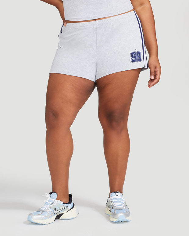 Plus sized model’s legs shown wearing heather grey micro short with 2 contrasting navy blue stripes down both sides. Short features navy blue Baby Phat cat 99 heritage logo on wearer's left thigh. 
