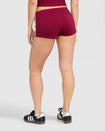 Back view image of standard sized model’s legs shown wearing burgundy micro short with 2 contrasting off white stripes down both sides. 