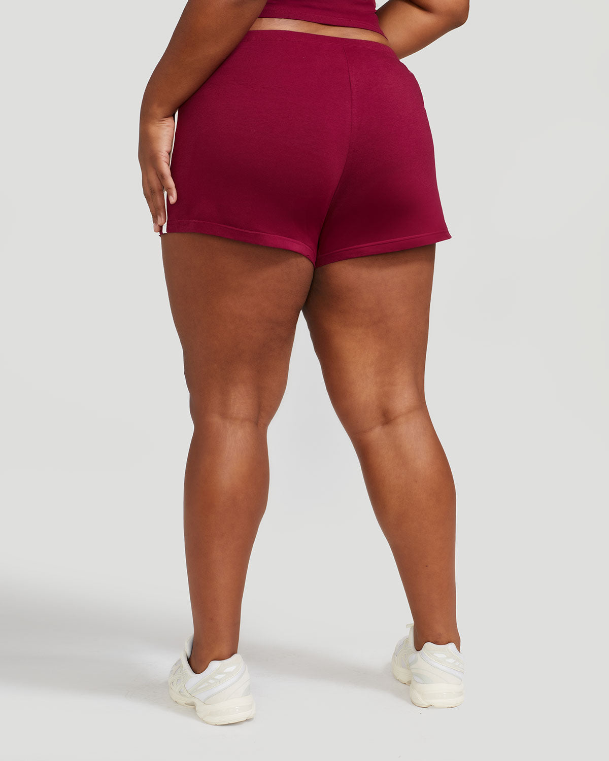 Back view image of plus sized model’s legs shown wearing burgundy micro short with 2 contrasting off white stripes down both sides. 