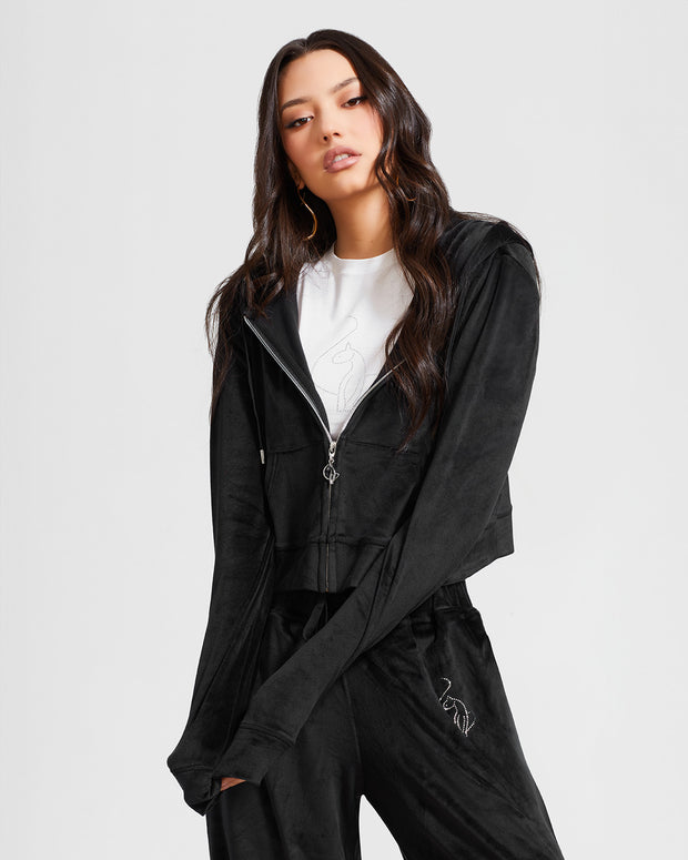 Standard sized model shown wearing black velour zip up hoodie with matching wide leg sweatpants. Zippered sweatshirt features rhinestone Baby Phat script logo on upper chest and oversized rhinestone cat logo on the back. Sweatshirt features silver cat logo zipper pull.